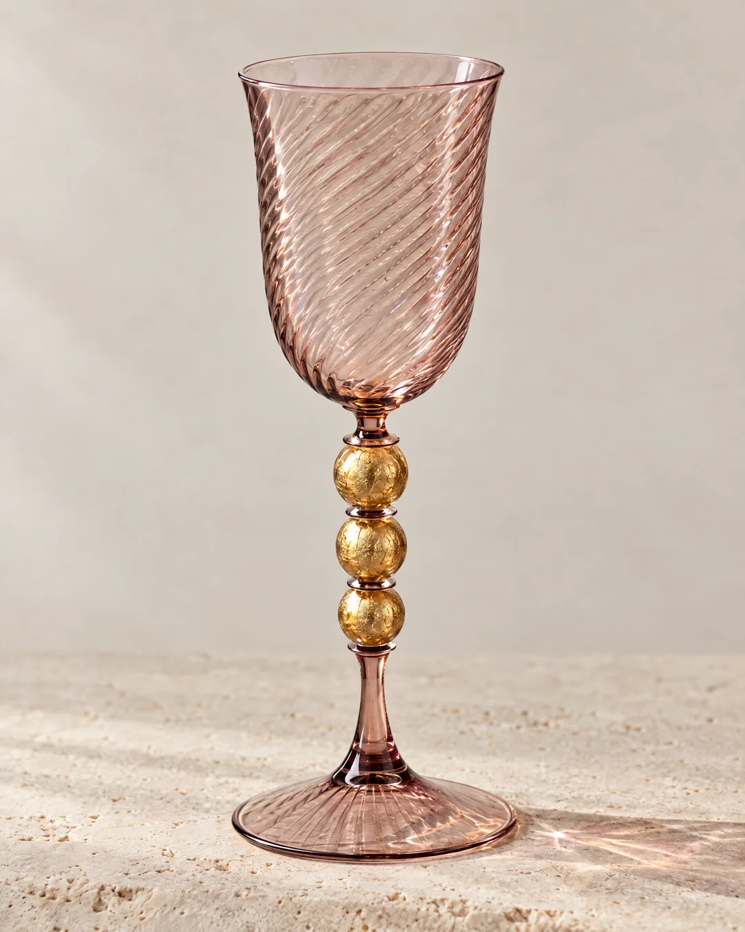 A rose-tinted hand-blown goblet with a spiral-ribbed bowl and gold-leaf knops on its stem