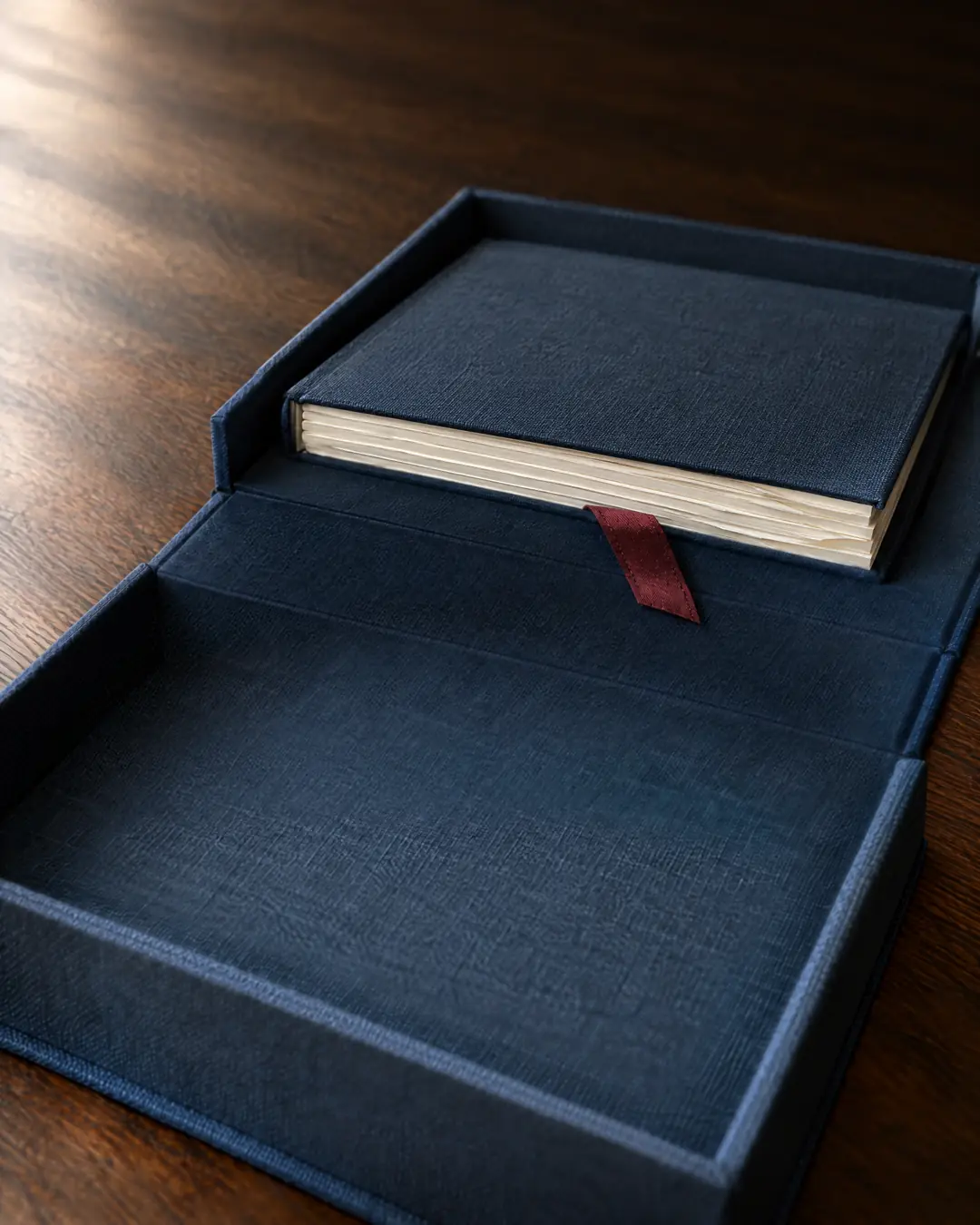 An open slate-blue cloth box, its near compartment empty, a slim cloth-bound book of letters resting in the far one