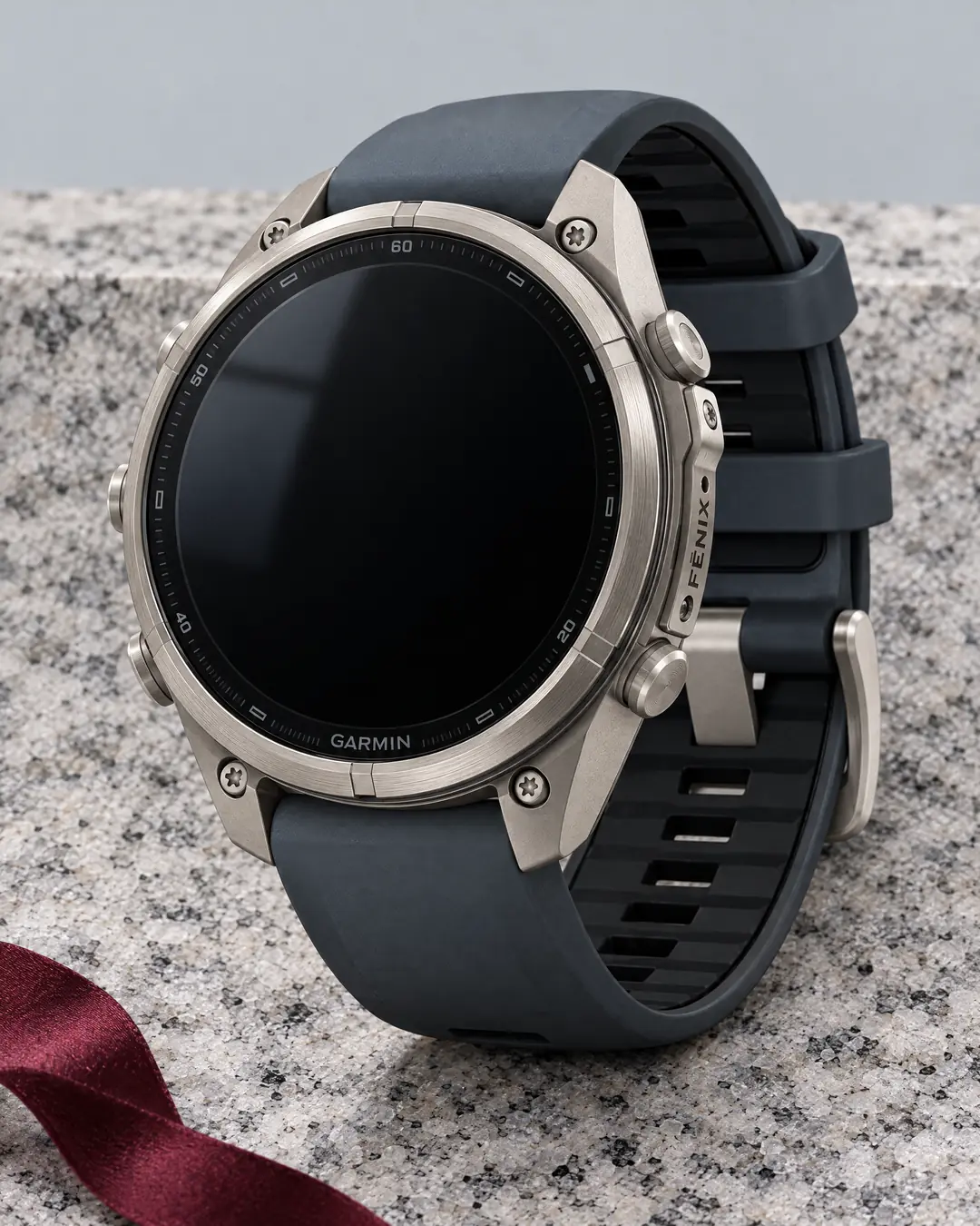 A Garmin titanium GPS watch with a dark sapphire screen and graphite strap on pale granite