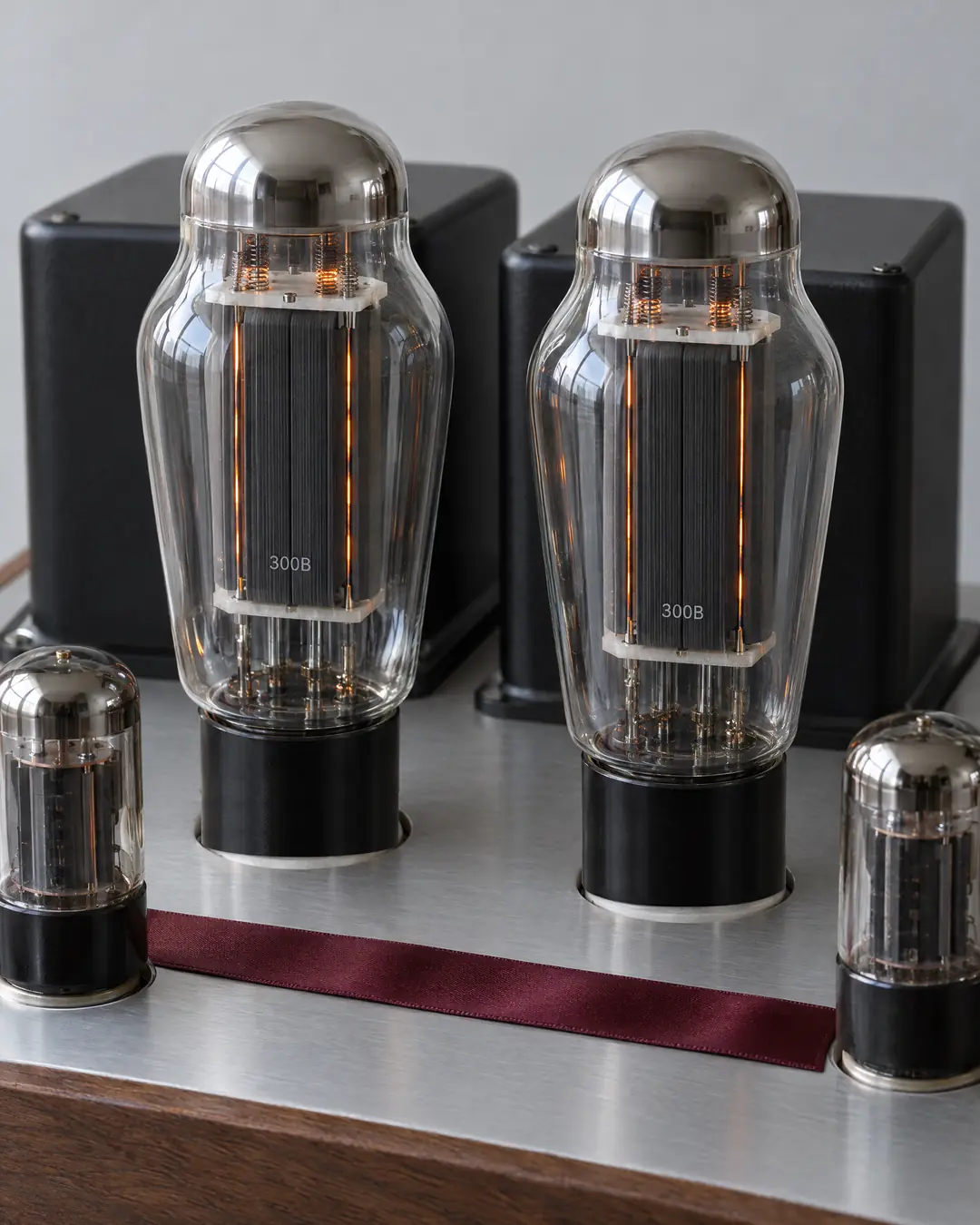 Two 300B valves glowing softly on the brushed aluminum top of a hand-built valve amplifier, with black transformers behind and a walnut base