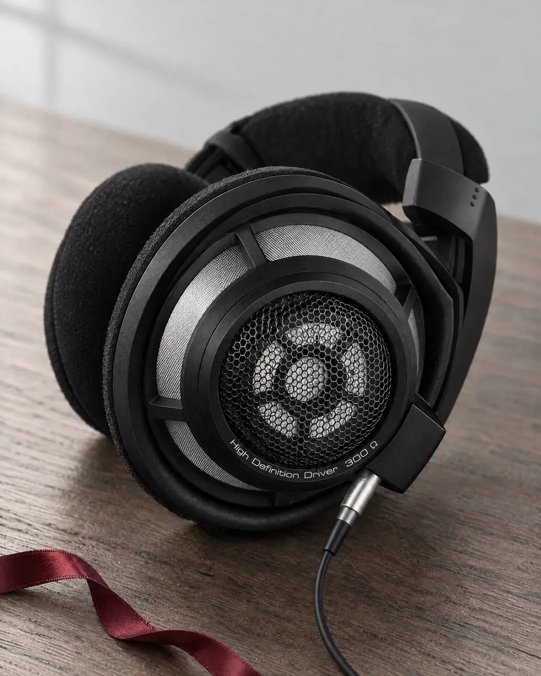 Open-back reference headphones on oak, the angled ring driver visible through a fine honeycomb grille
