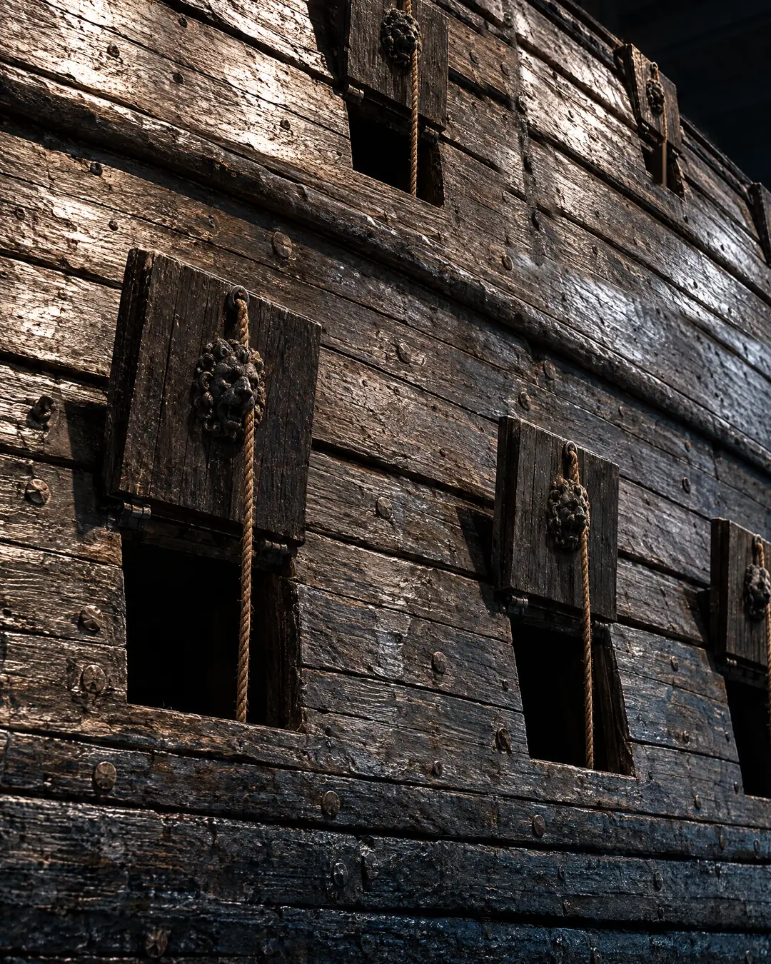 The near-black oak hull of the warship Vasa in the museum's dim hall, its square gunports open beneath raised lids carved with lion masks.