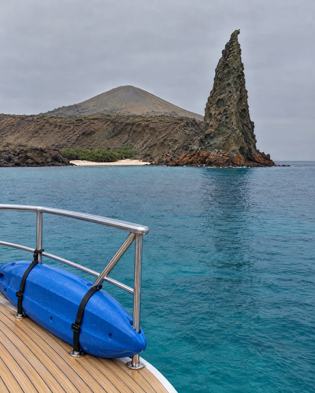 Pinnacle Rock on Bartolomé in the Galápagos, seen past a blue kayak on the teak bow of an expedition yacht at anchor