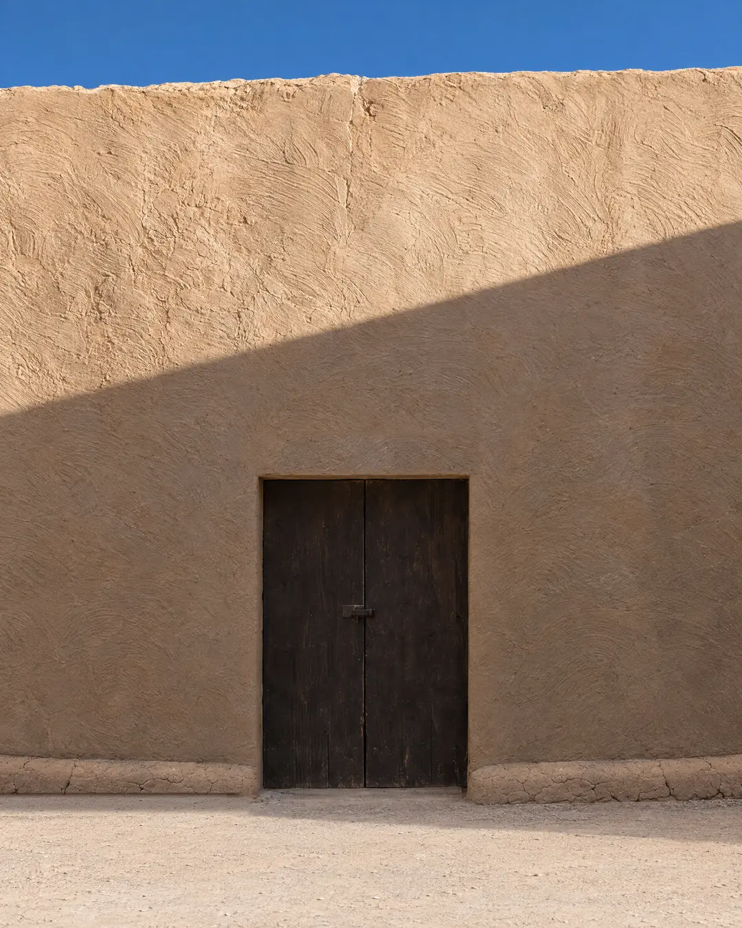 The dark wooden patio door in the long adobe wall of Georgia O'Keeffe's courtyard at Abiquiú, in clear afternoon light