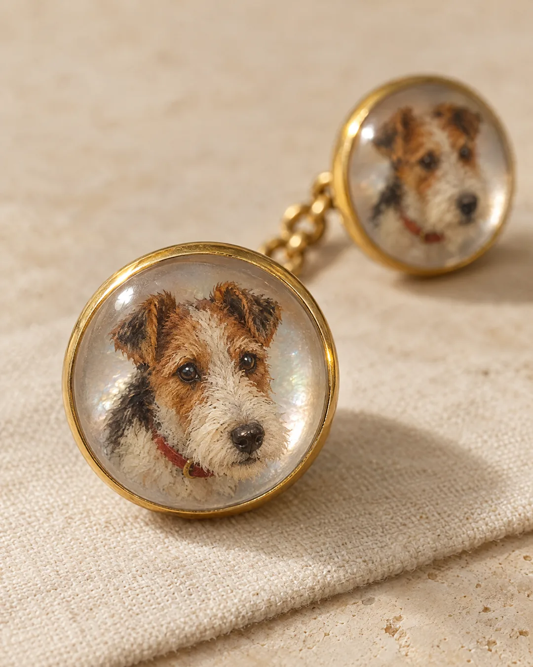A gold cufflink with two rock-crystal faces joined by a short chain, each reverse-painted with a wire fox terrier